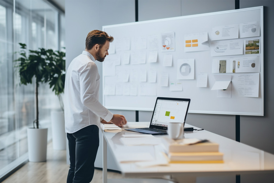 Stockphoto of a man standing by a whiteboard and brainstorming ideas, laptop next to him, simple open office environment, minimalistic nordic design, corporate, scandinavian, symmetry, photorealism